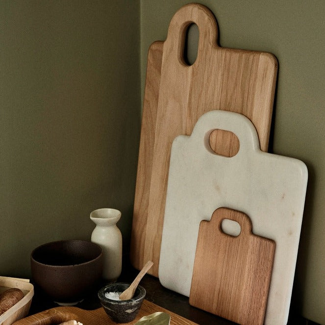 Stack of oak chopping boards up against a green wall.