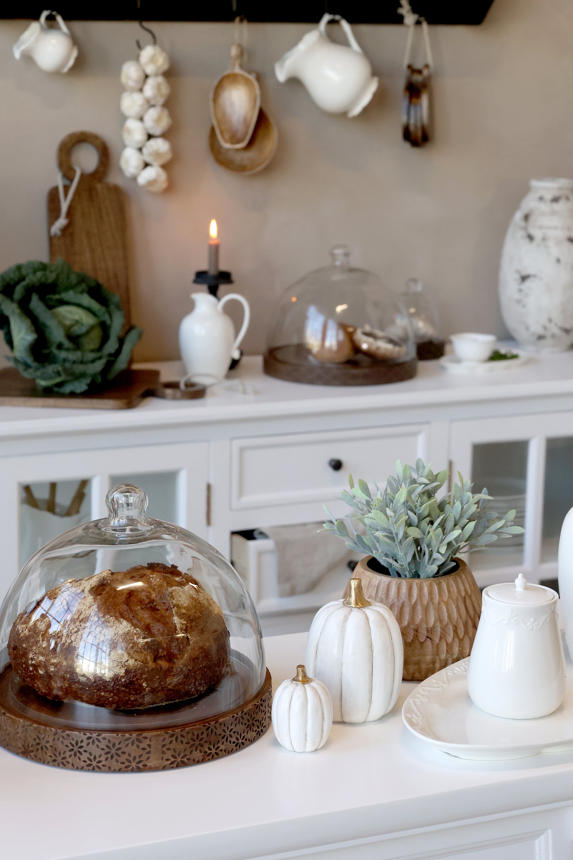 Wood and glass domes in kitchen with bread inside, styled with autumn themed decorations.