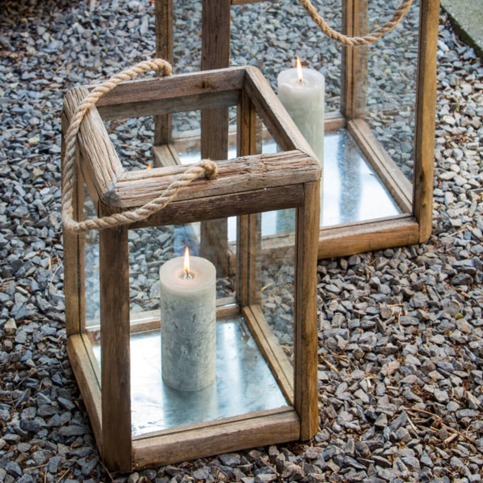 Set of two wooden candle lanterns outside on pebble ground with lit candles inside.