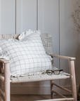 A grid print white ruffle cushion sits on a woven armchair.