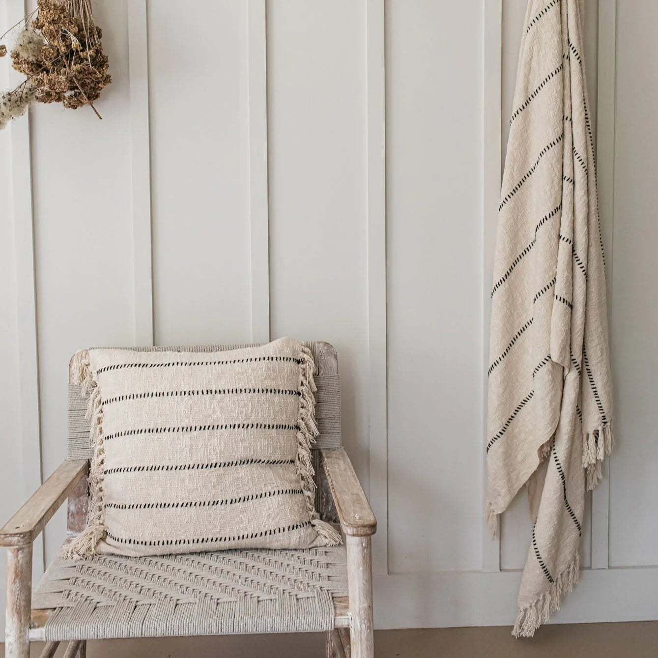 A striped linen cushion on a woven armchair, matching striped blanket hangs from the wall to the right.
