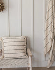 A striped linen cushion on a woven armchair, matching striped blanket hangs from the wall to the right.