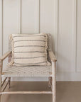 Striped neutral cushion sits on a woven armchair against a cream panelled wall.