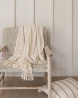 A striped neutral throw blanket is draped over a woven armchair with a matching cushion on the floor.