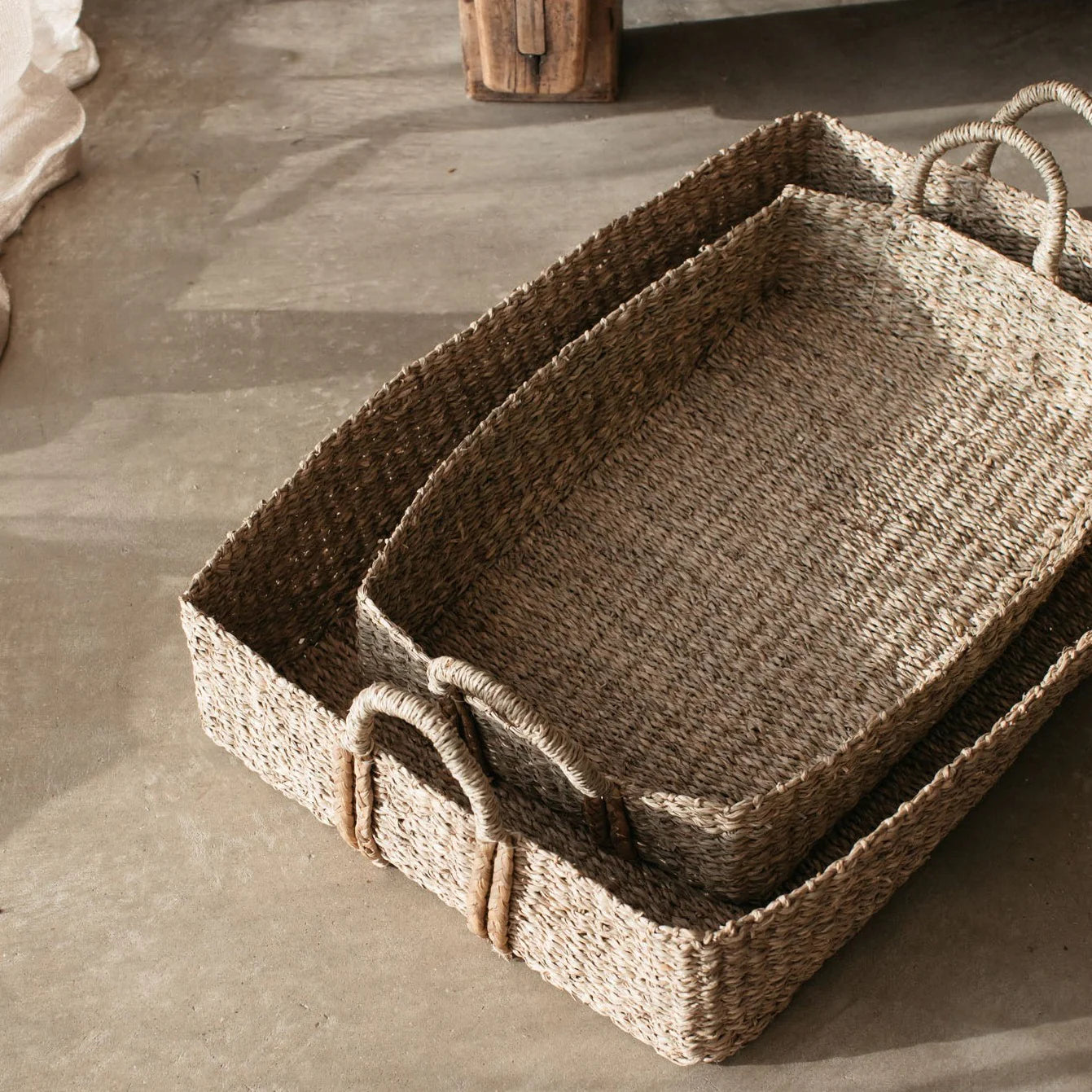 The Eliza Rectangular Seagrass Baskets stacked on a concrete floor.