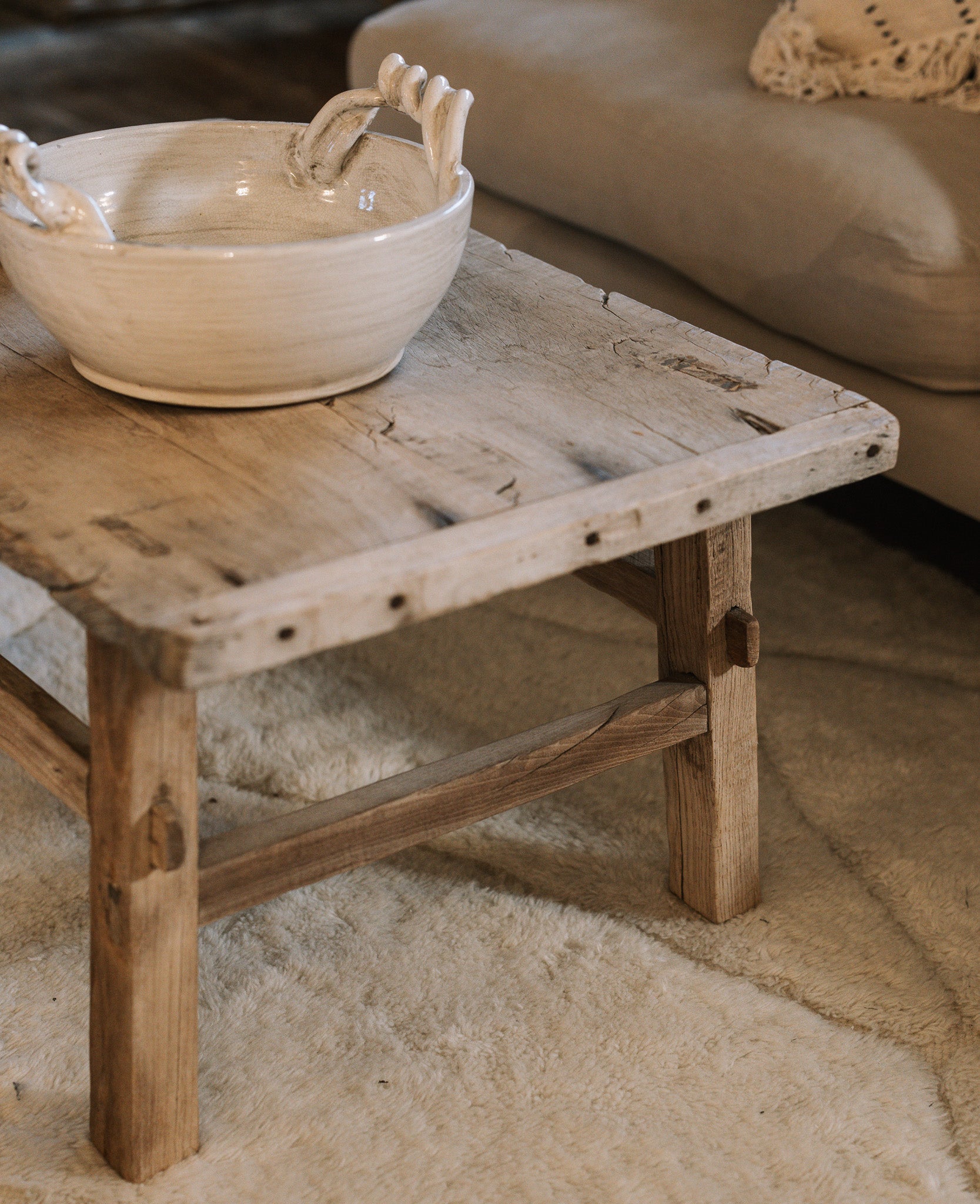 A Reclaimed Wood Coffee Table on white rug with ceramic bowl.