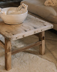 A Reclaimed Wood Coffee Table on white rug with ceramic bowl.