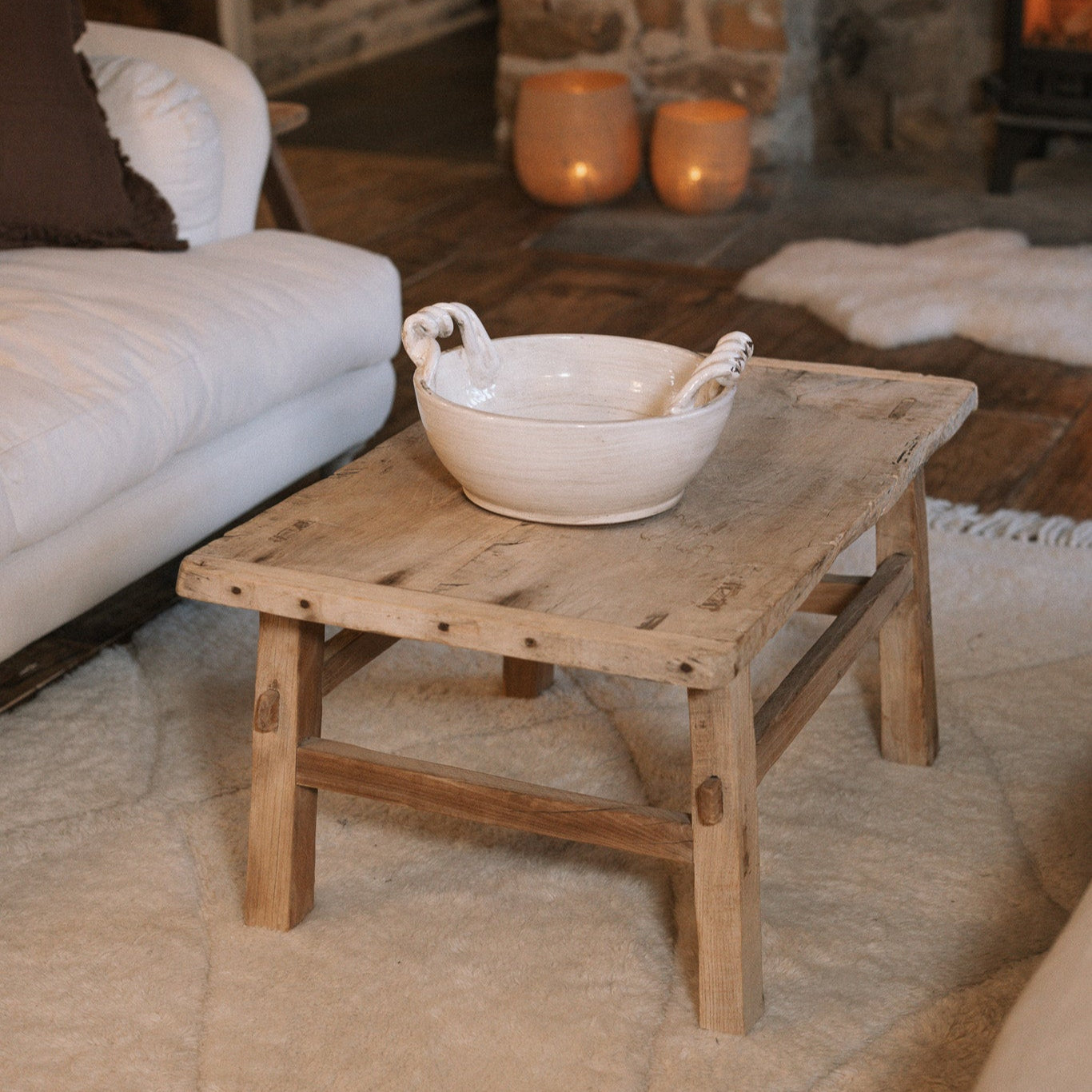 A Reclaimed Wood Coffee Table on white rug with ceramic bowl.