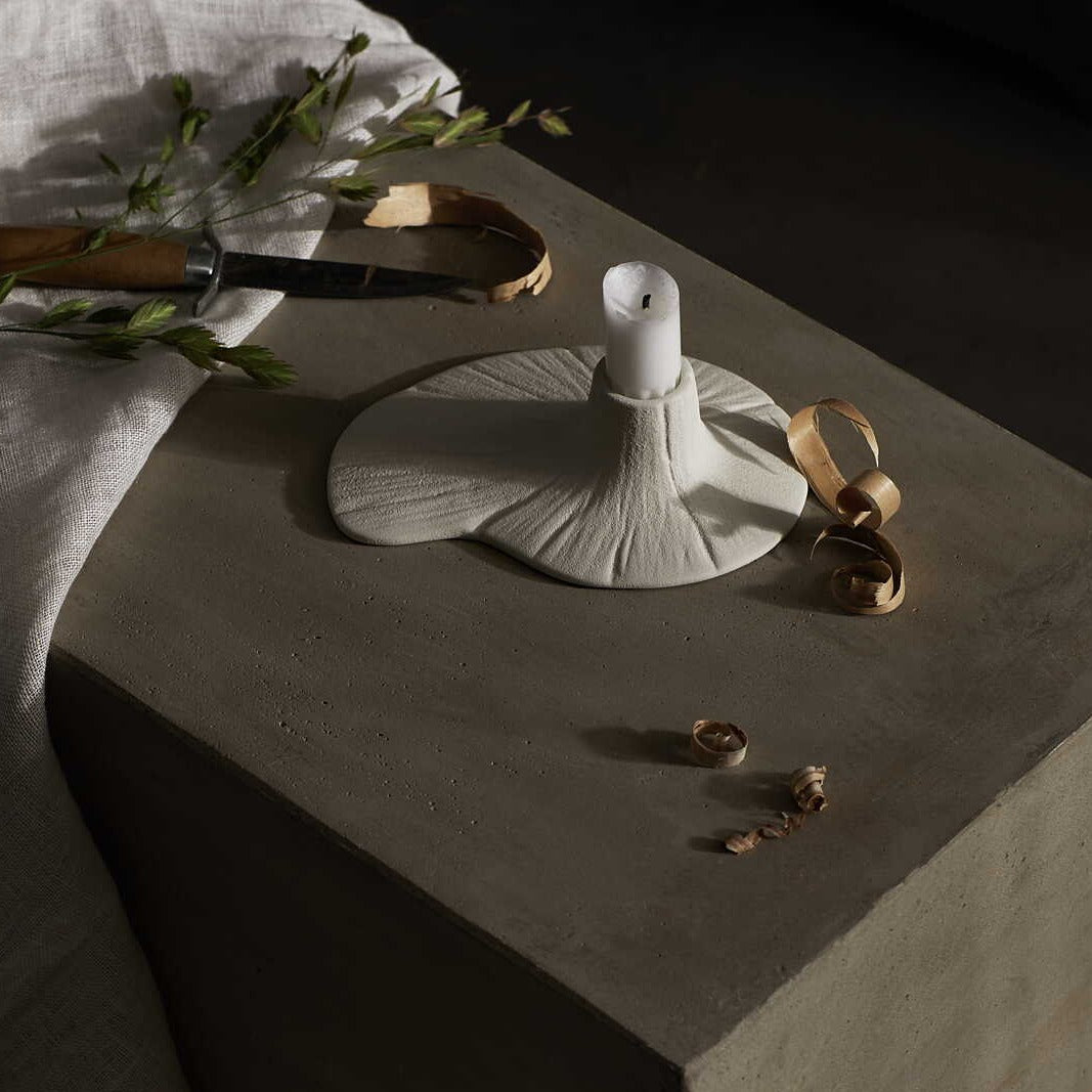 Milky white ceramic candle holder with white candle on stone table.