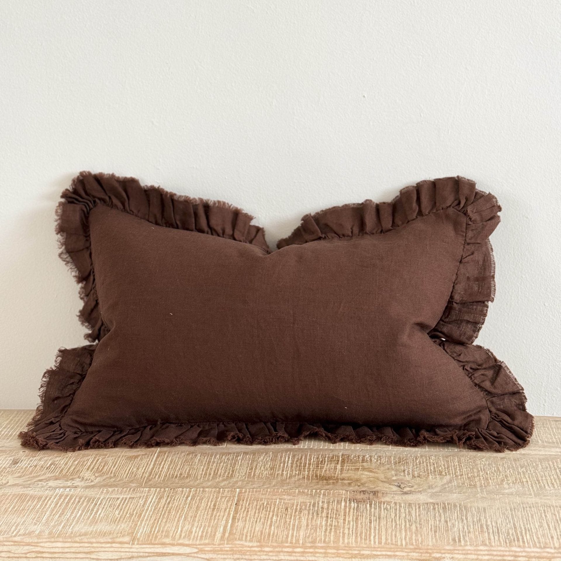 Chocolate brown rectangle linen cushion with ruffle edge on wooden surface.