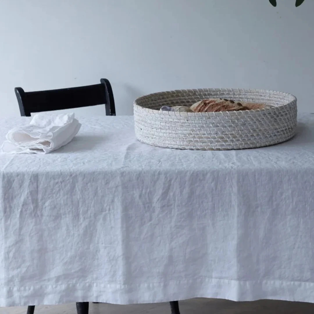 Linen white table cloth draped over a table, with a white woven basket on top.