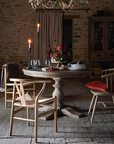 Wooden round dining table in large stone room, with candelabras, cushions and tableware.