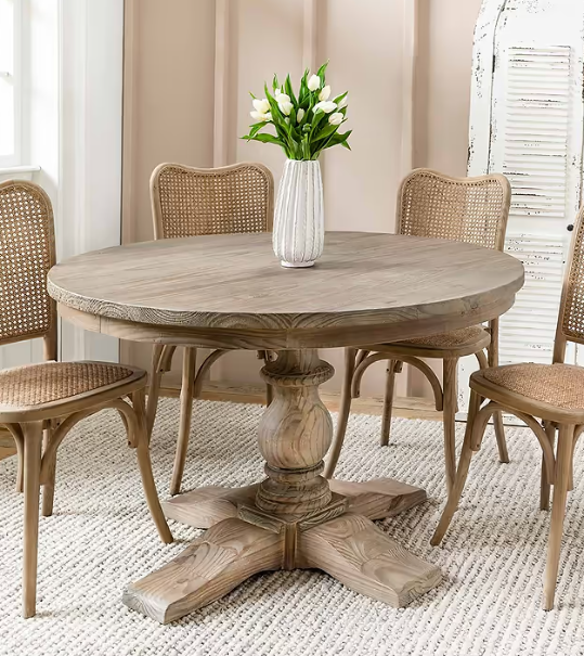 Large wooden round dining table with white vase on, with 4 rattan chairs around.