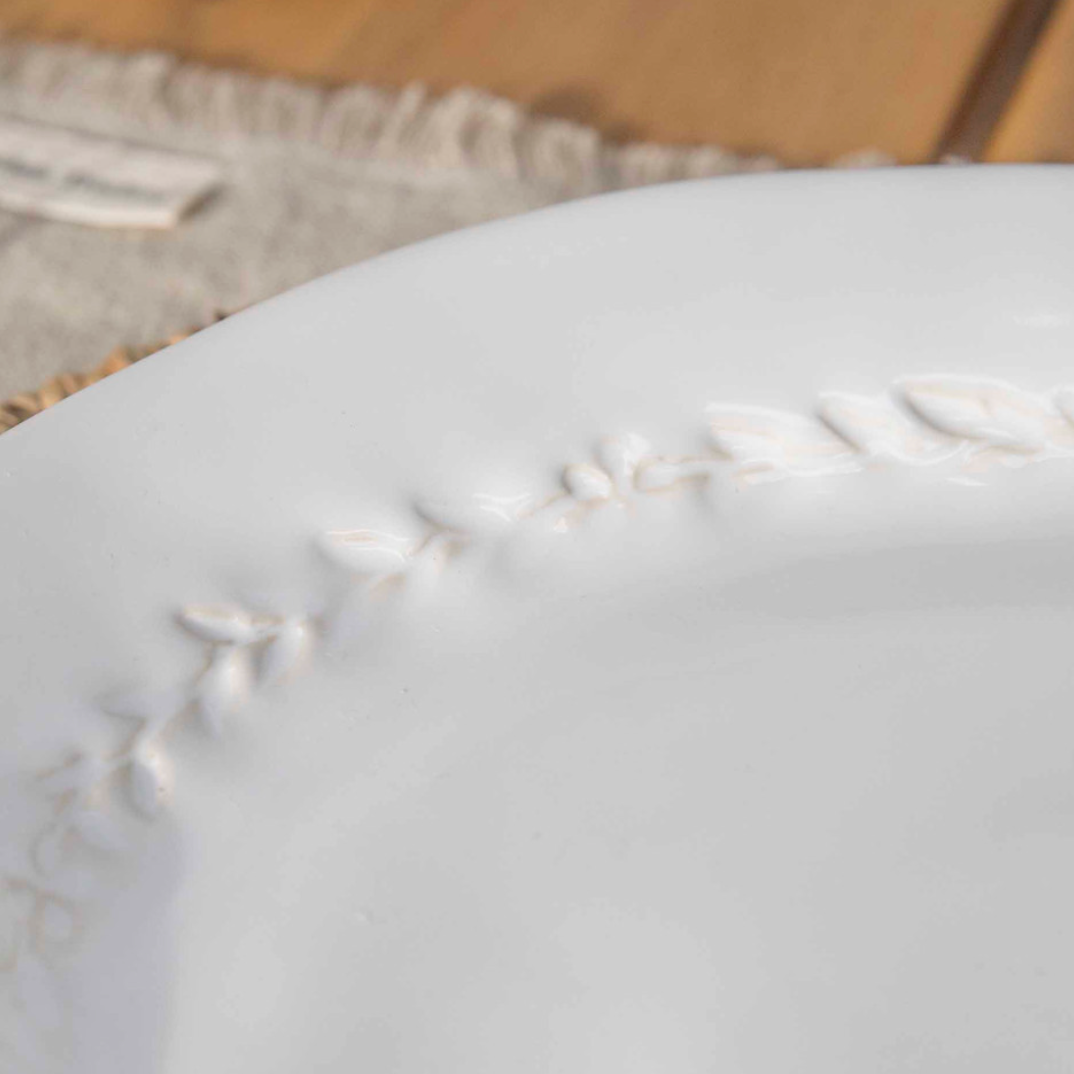 Close up of leaf detailing on white dinner plate.