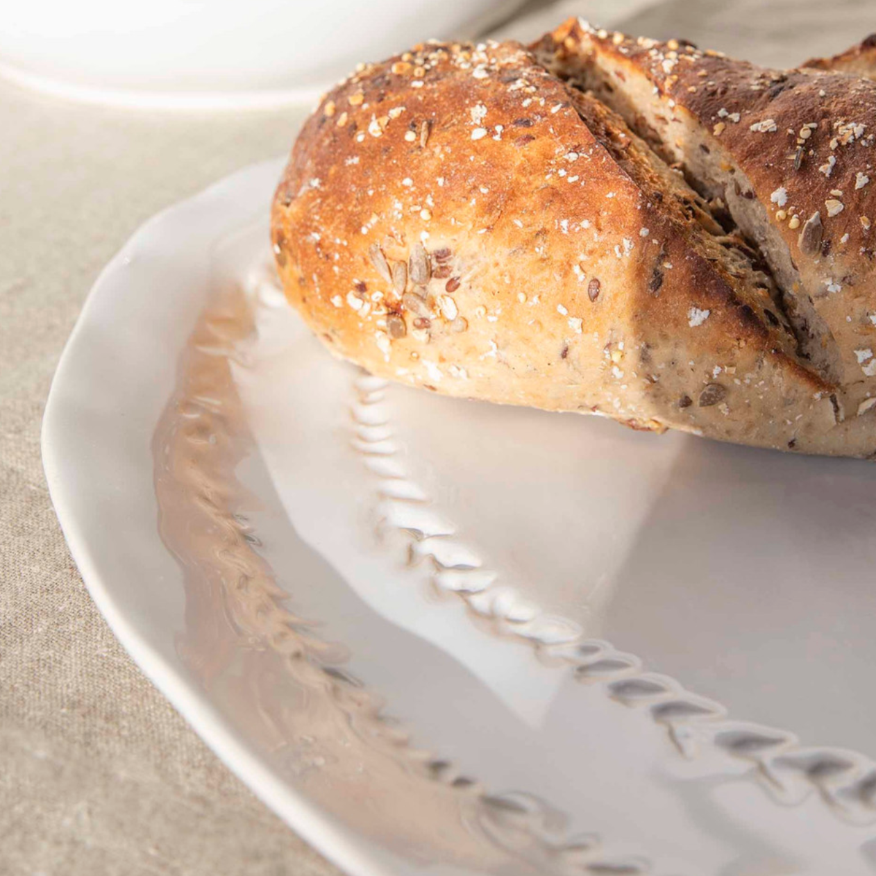 Close up of leaf detailing on white ceramic serving platter, with bread loaf on top.