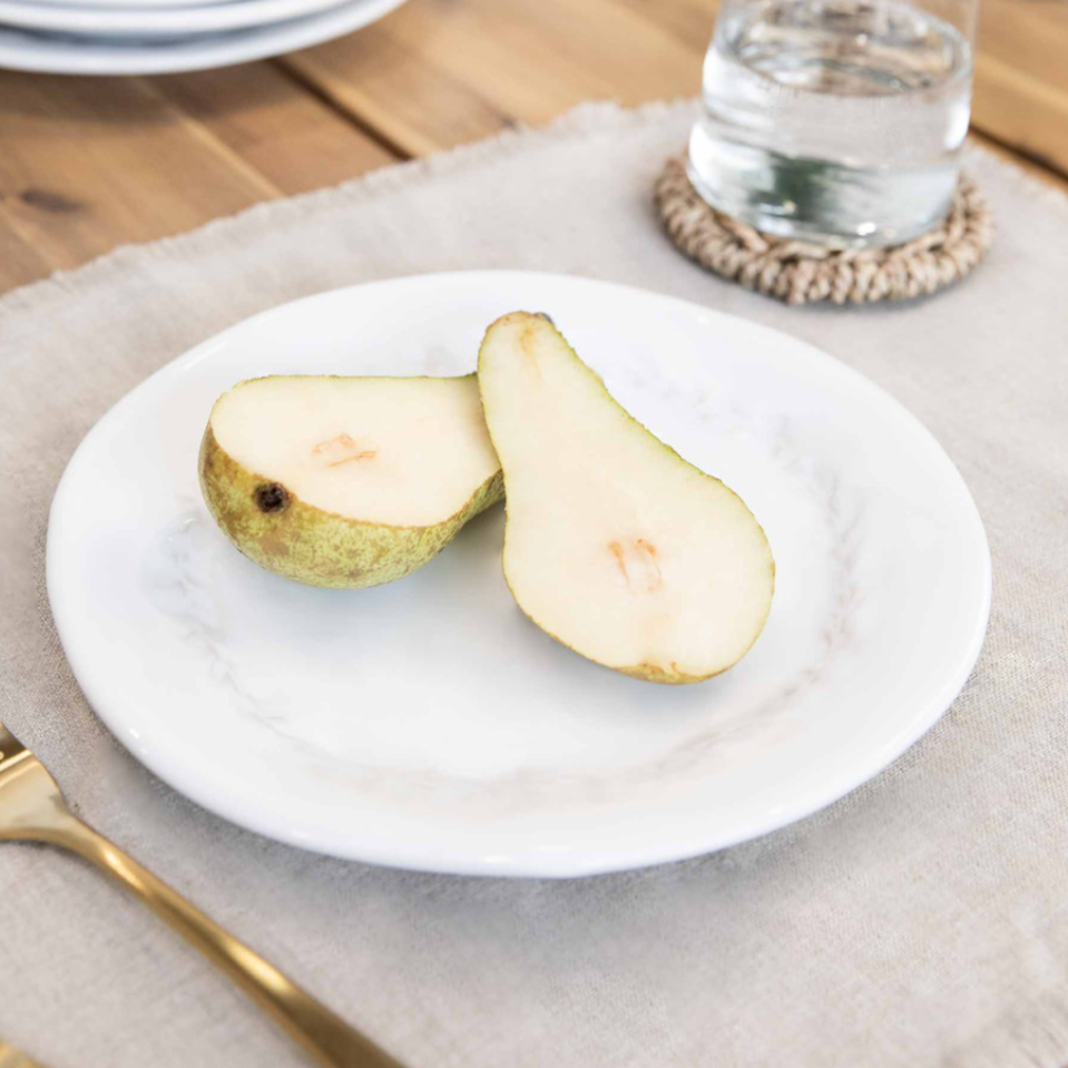 White ceramic side plate with a pear on, cut in half.