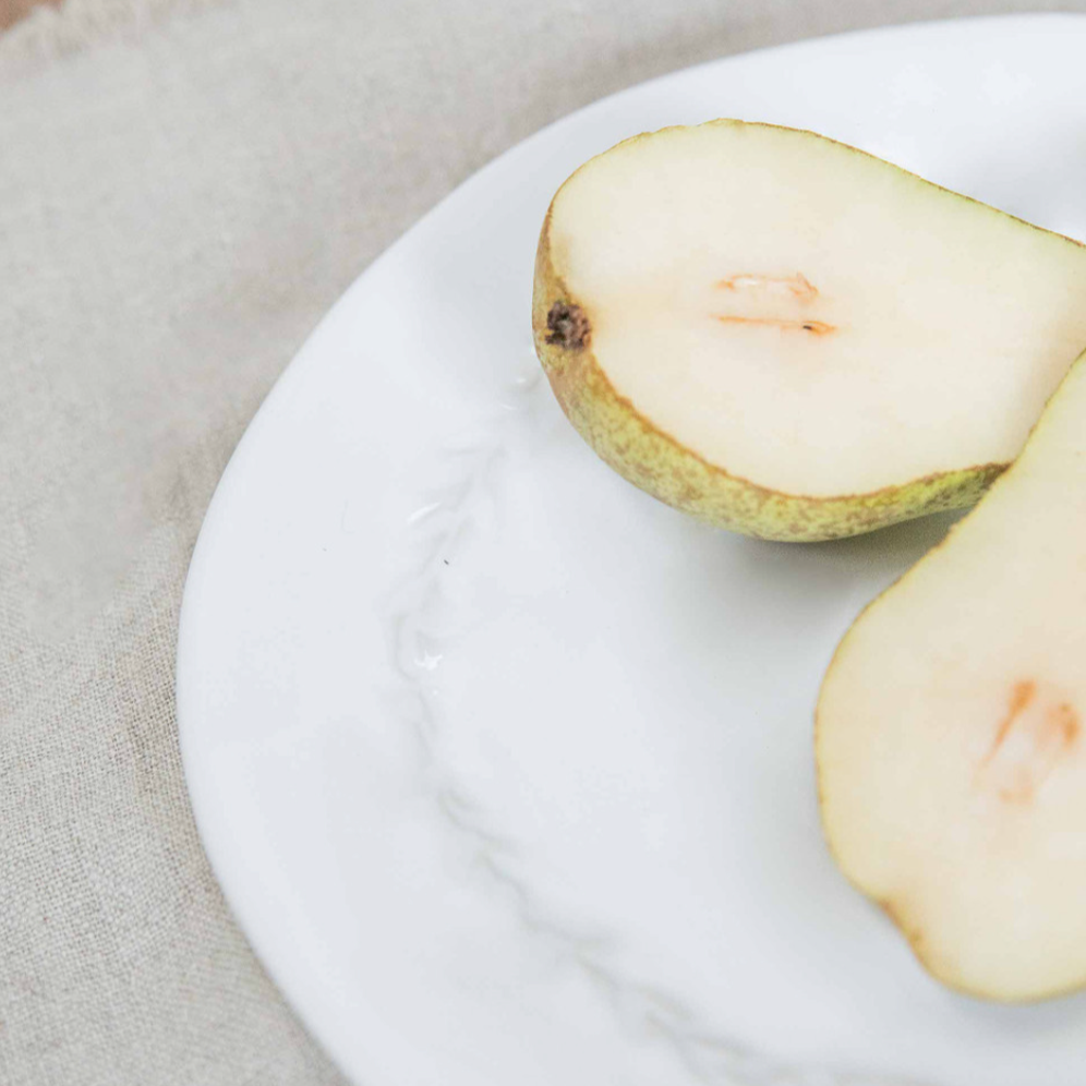 Close up ceramic white side plates with pear on top cut in half.