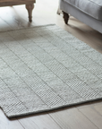 A small wool rug placed on wooden floor in living room.