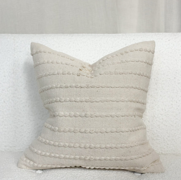 Cream embroidered cushion on a white sofa.