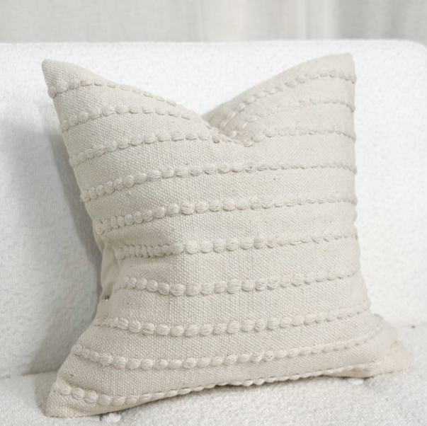 Cream embroidered cushion on a white sofa.