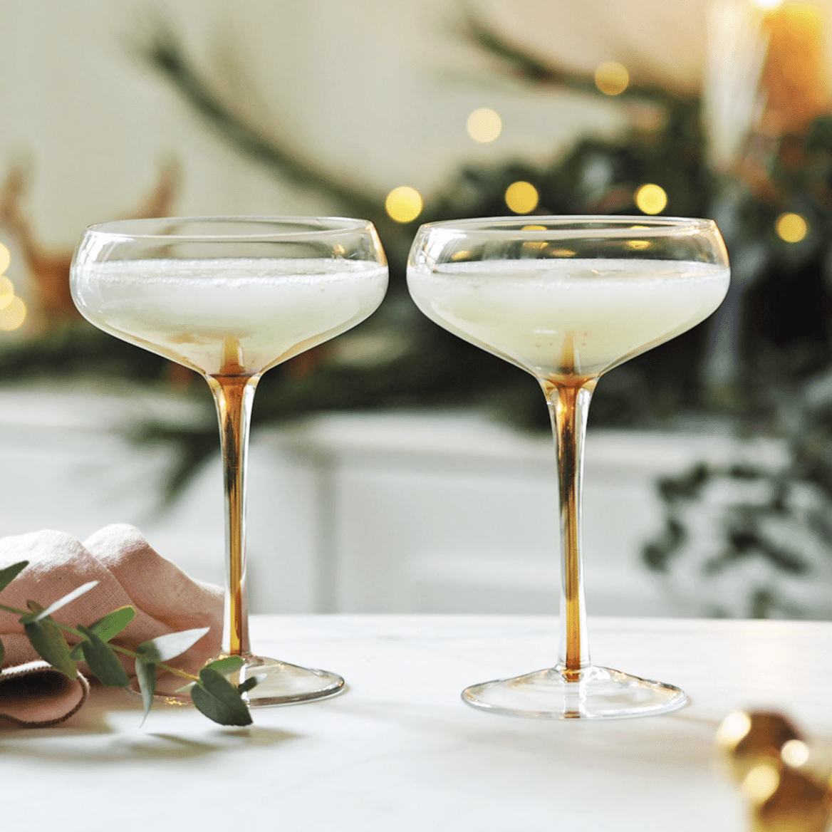 2 filled amber stemmed cocktail glasses on a kitchen top.