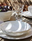 Pearly white pasta plate on top of dinner plate on outdoor dining table.