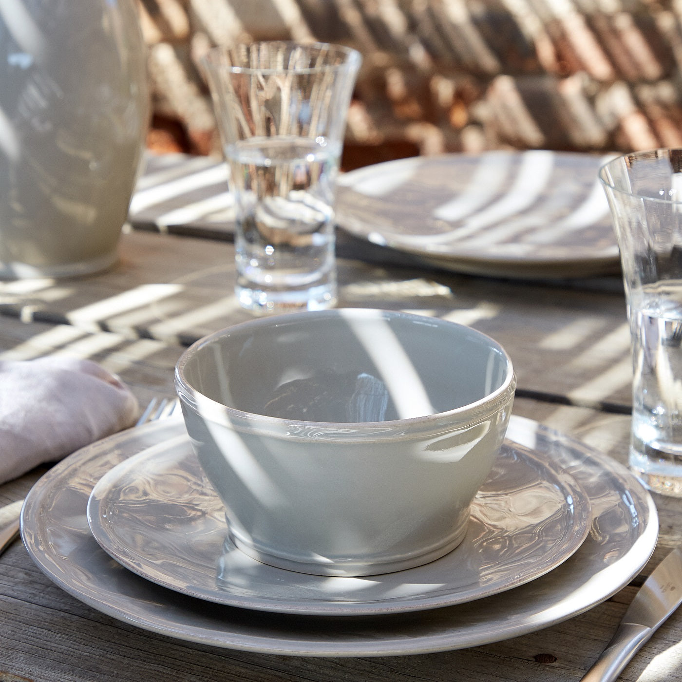 Stack of pearly white dinnerware on an outside dining table, including dinner plate, side plate, and cereal bowl.