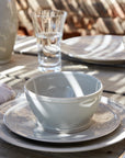Stack of pearly white dinnerware on an outside dining table, including dinner plate, side plate, and cereal bowl.