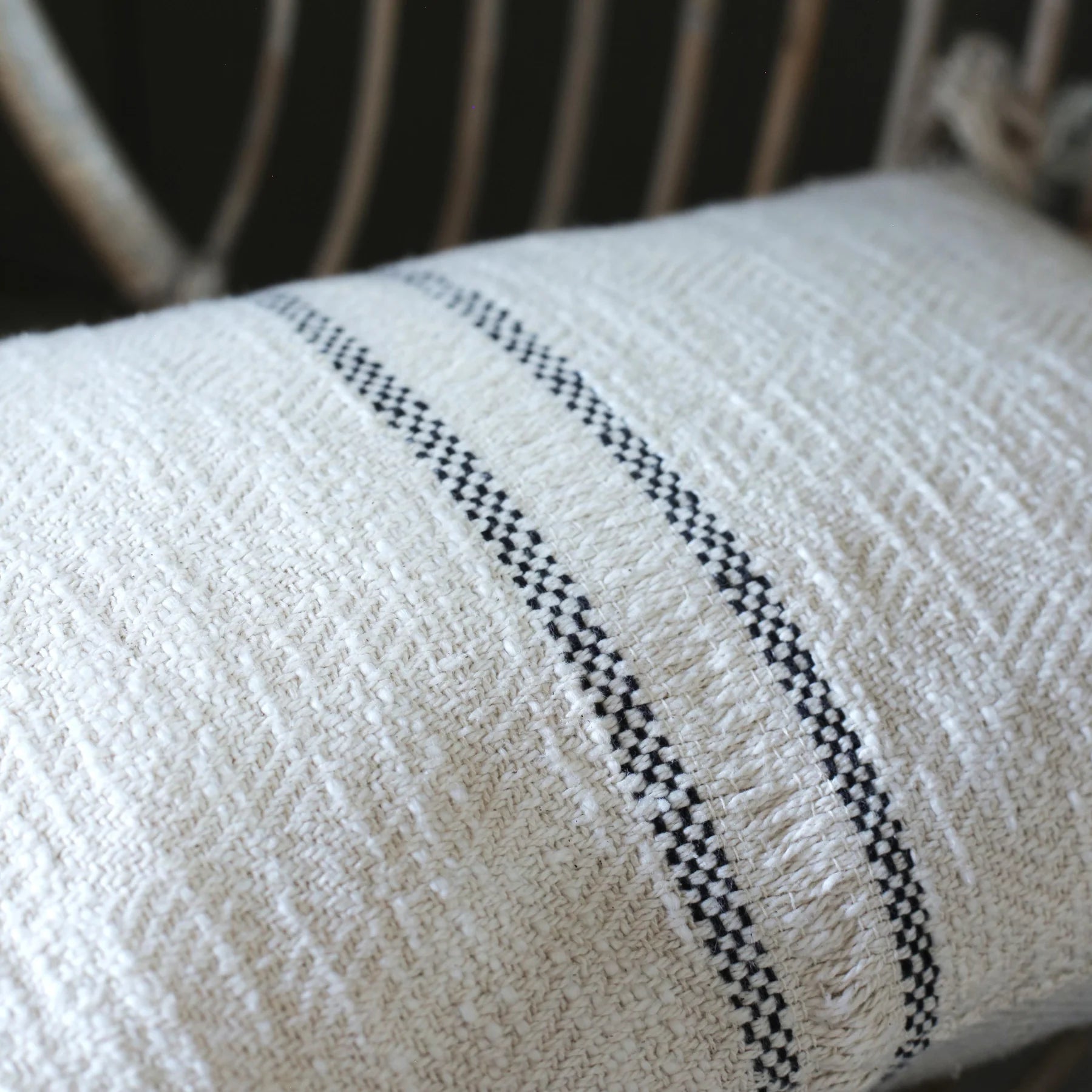 Textured Andas cream cotton cushion with slate grey stripe on a rattan chair.