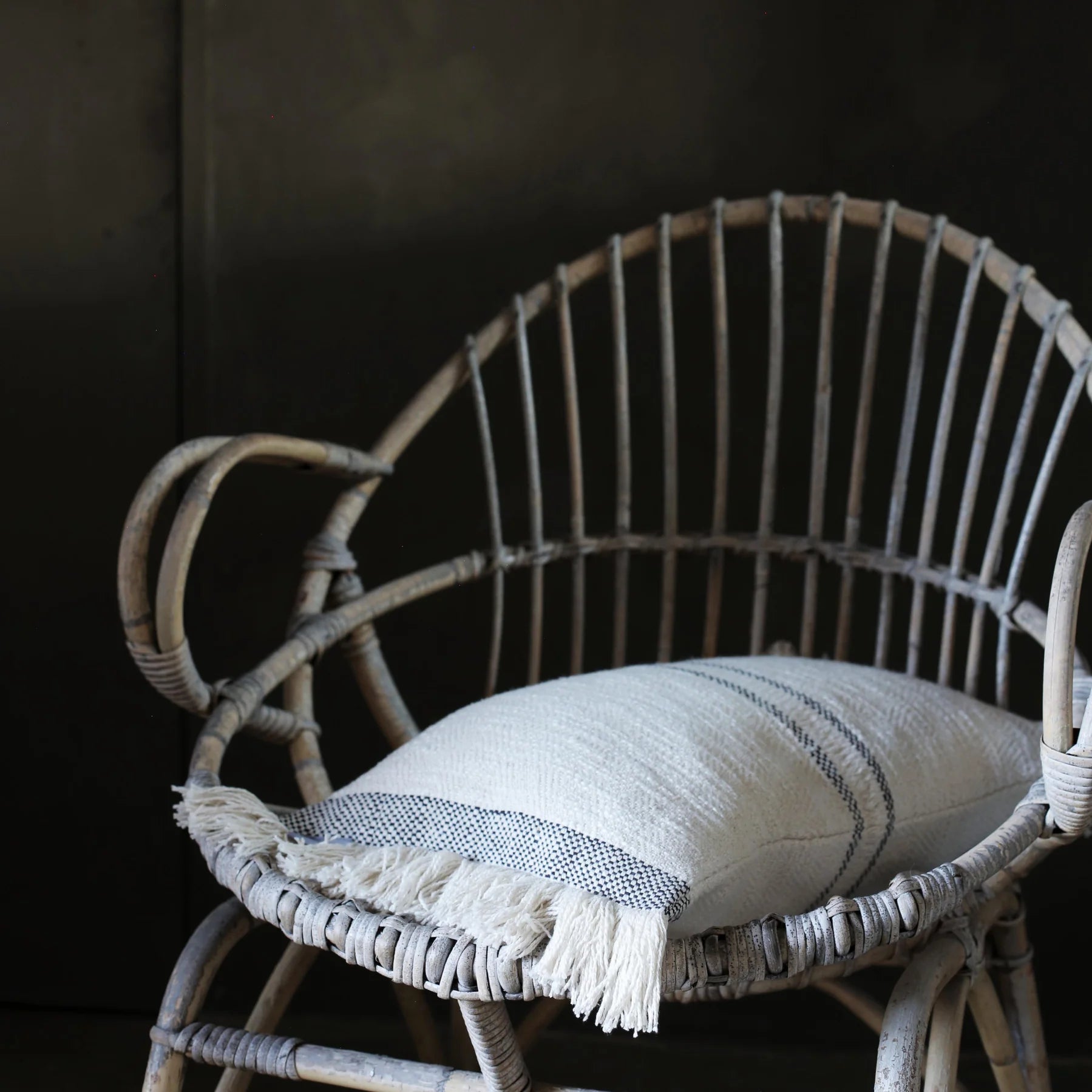 Andas cotton cushion with slate stripe on a rattan chair against a dark brown background.