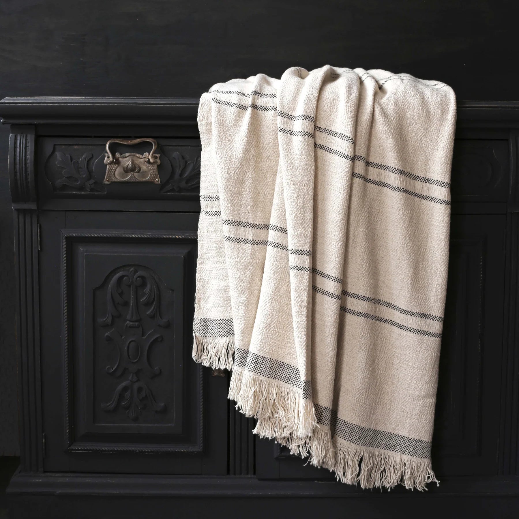 Draped cotton throw blanket with slate stripes on a painted black table.