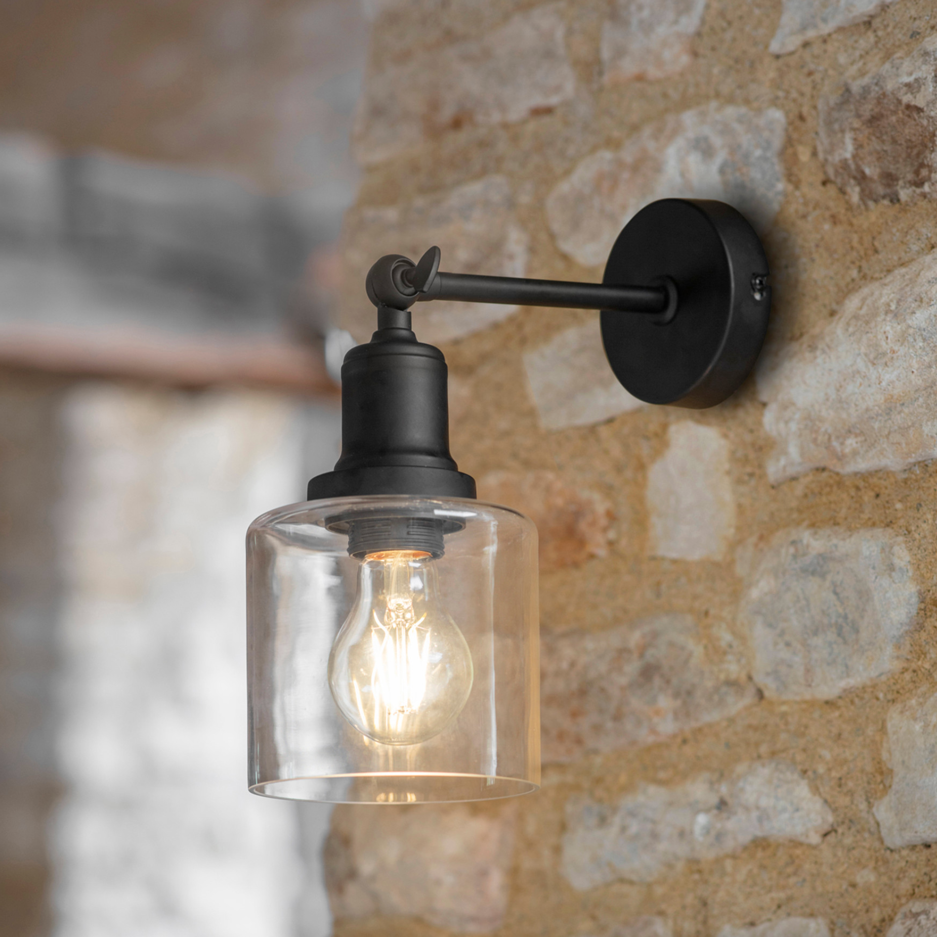 Black wall light with glass shade on stone wall. 