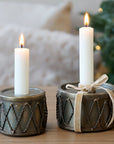 Drum shaped candlestick holder with two lit candles and a bow around.