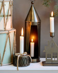 Drum shaped candlestick holder with lit candle inside, a bow and other surrounding Christmas decorations.