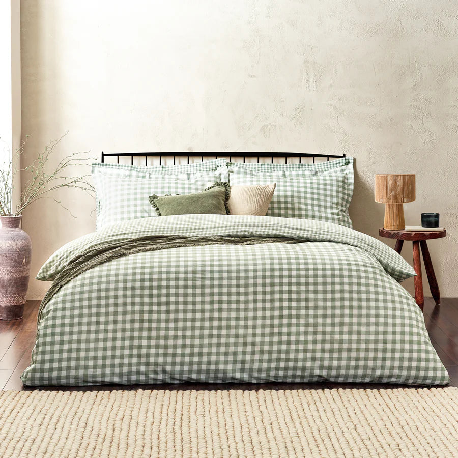 Forest green gingham bedding set on bed with throw and cushions, with bedside table and vase.