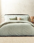 Forest green gingham bedding set on bed with throw and cushions, with bedside table and vase.