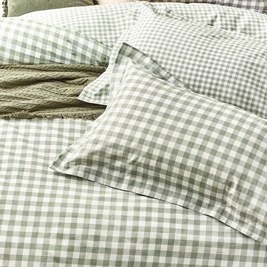 Close up of forest green gingham bedding set on bed with throw and cushions, with bedside table and vase.