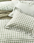 Close up of forest green gingham bedding set on bed with throw and cushions, with bedside table and vase.