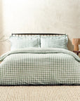 Forest green gingham bedding set on bed, with bedside table and vase.