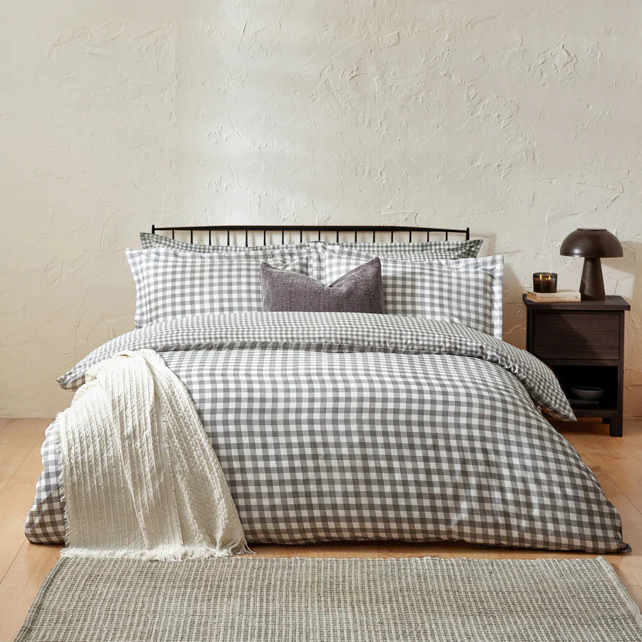 Grey gingham bedding set on bed with throw and grey cushion, with bedside table.