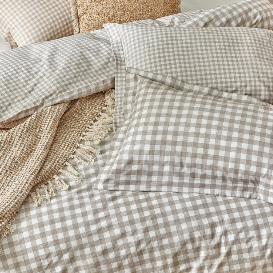 Close up of natural gingham bedding set on bed with cushion and throw.