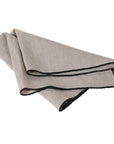 Natural linen napkin with black edge folded over.