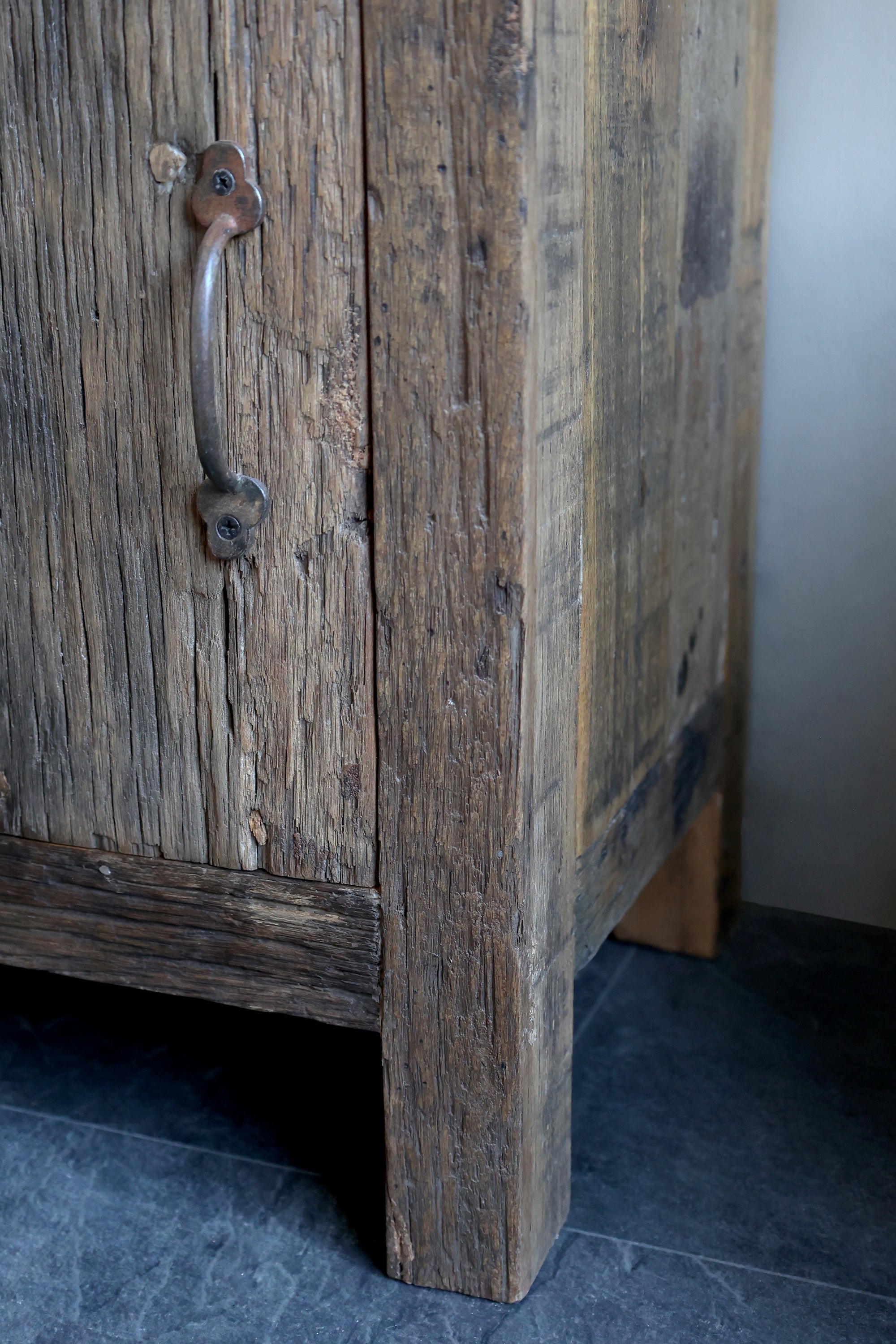 Close up of leg and patina finish on reclaimed wooden cabinet with one drawer and one door.