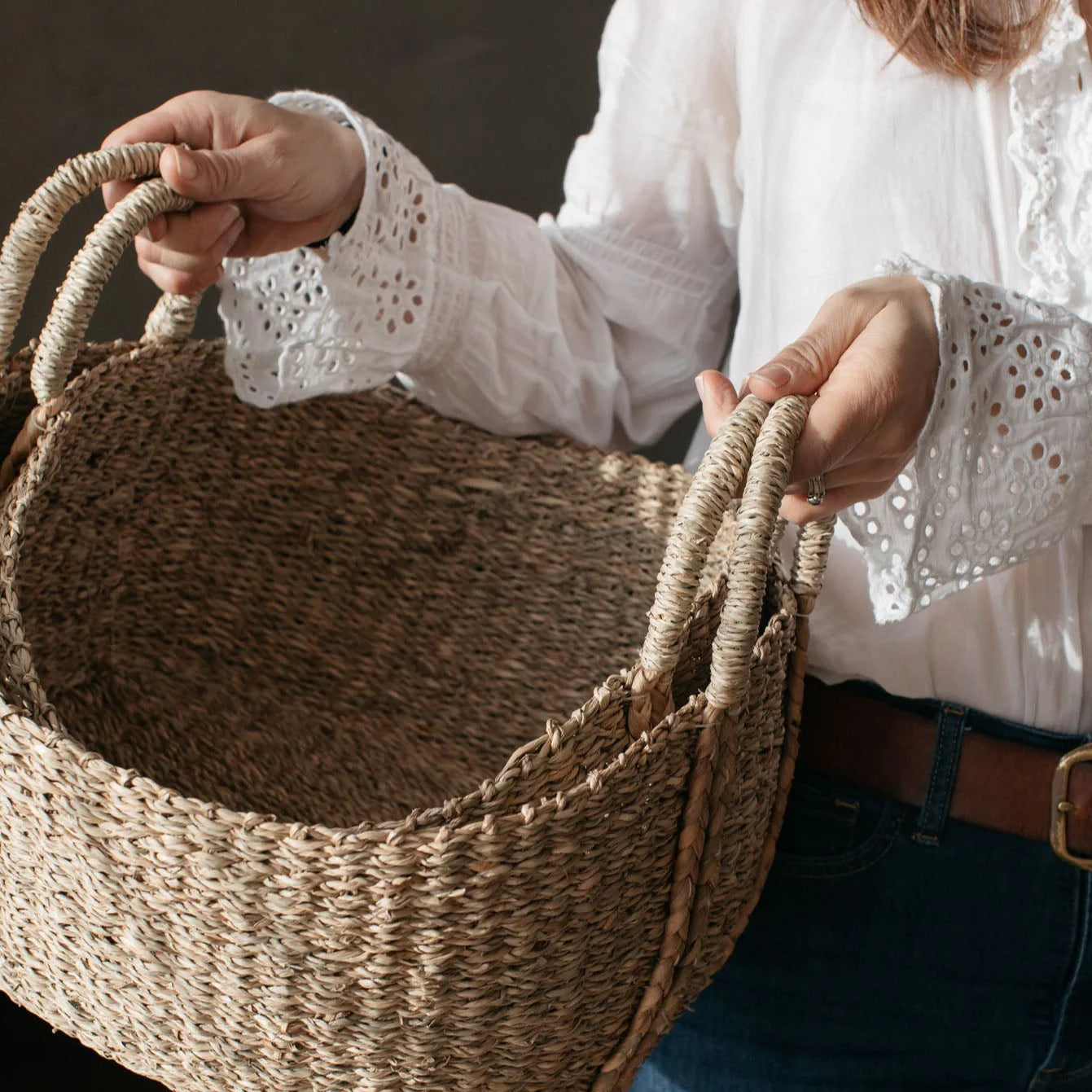 Woman in white linen shirt holding two seagrass baskets.