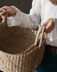 Woman in white linen shirt holding two seagrass baskets.
