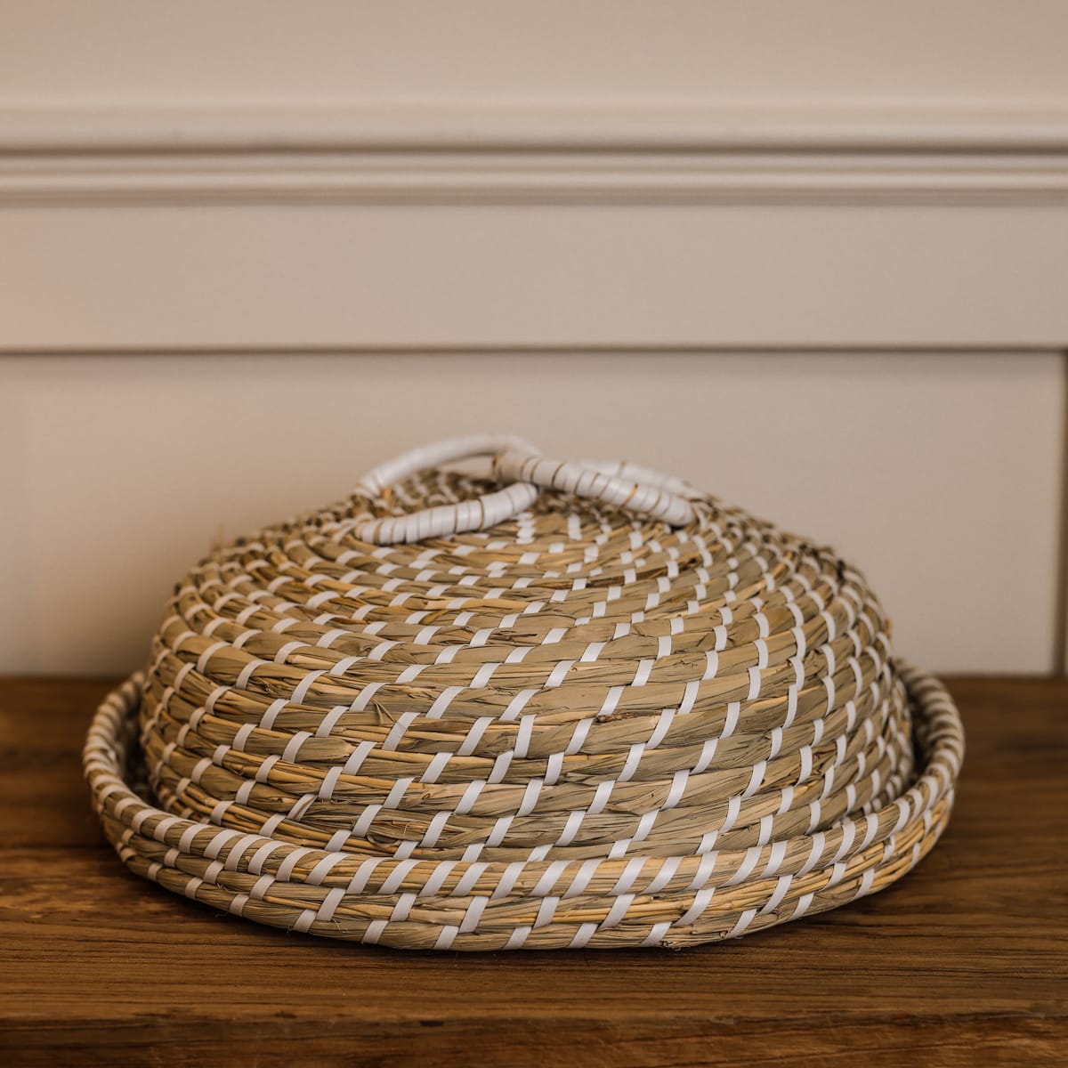 Woven seagrass cake dome with white loops and wooden console.