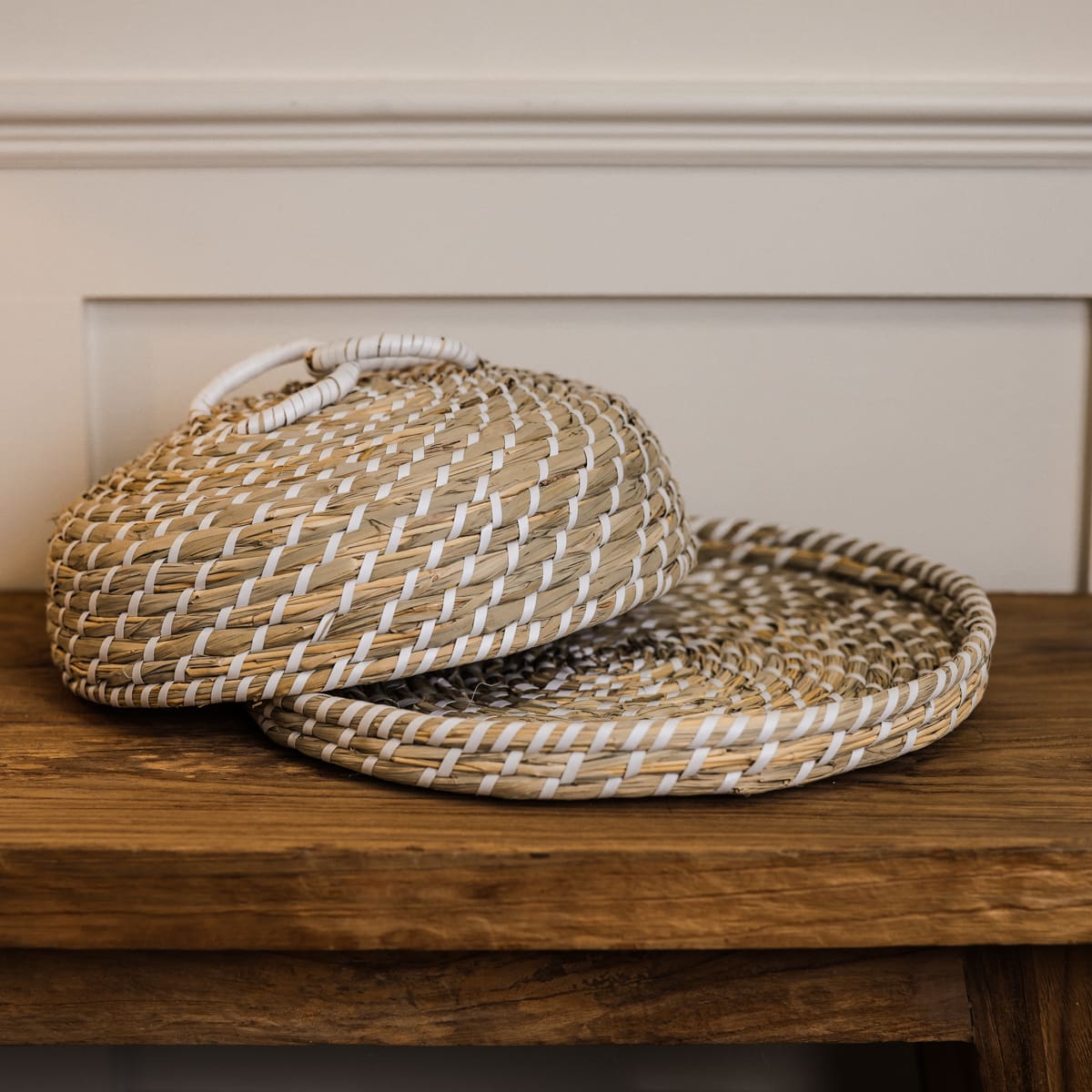 Woven seagrass cake dome with top slightly ajar on wooden console. 