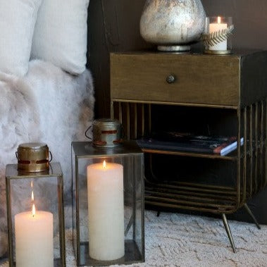 Two glass and brass candle lanterns with large candles inside styled in bedroom.