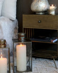 Two glass and brass candle lanterns with large candles inside styled in bedroom.