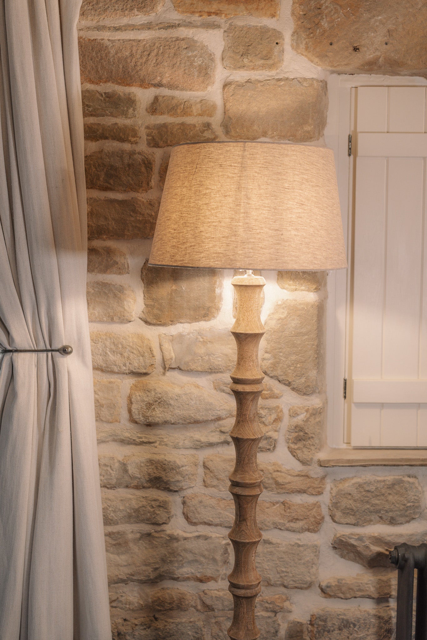 Bamboo look wooden floor lamp with linen shade against stone wall.